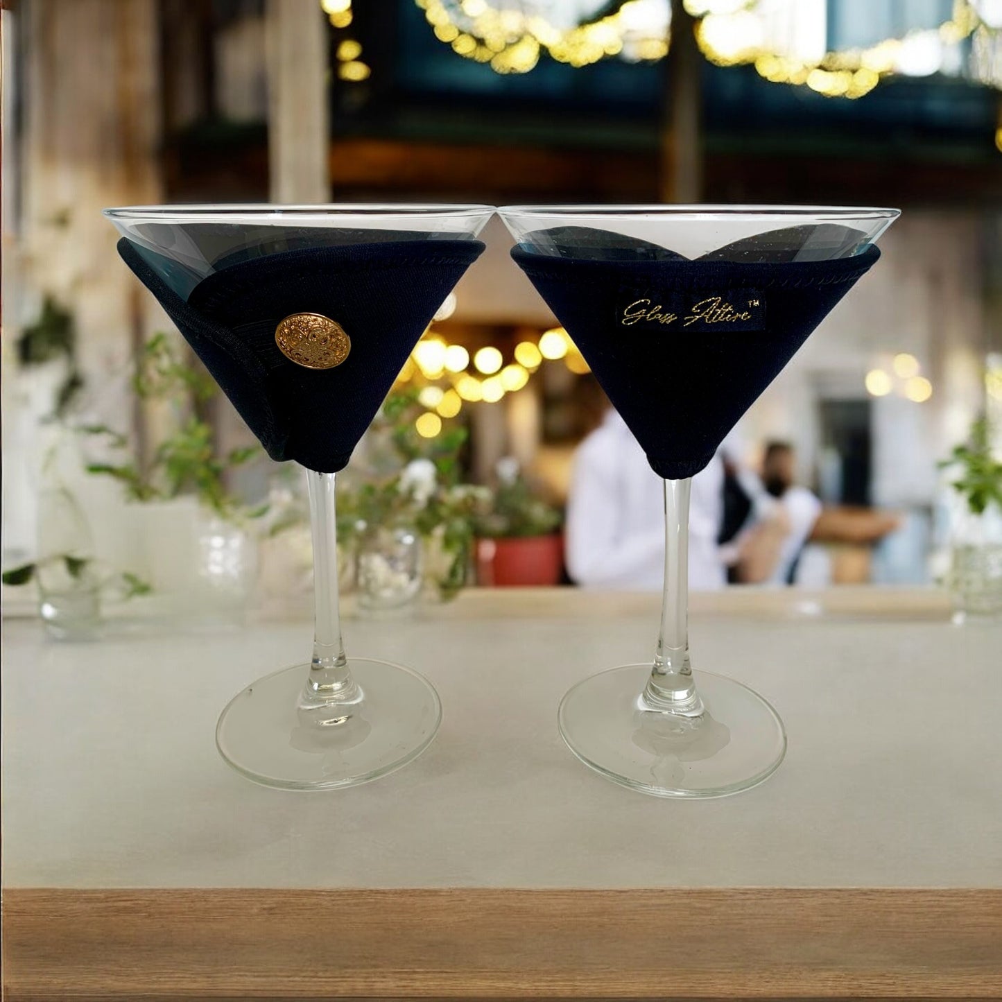 Two black cocktail glasses with gold buttons on a bar counter.