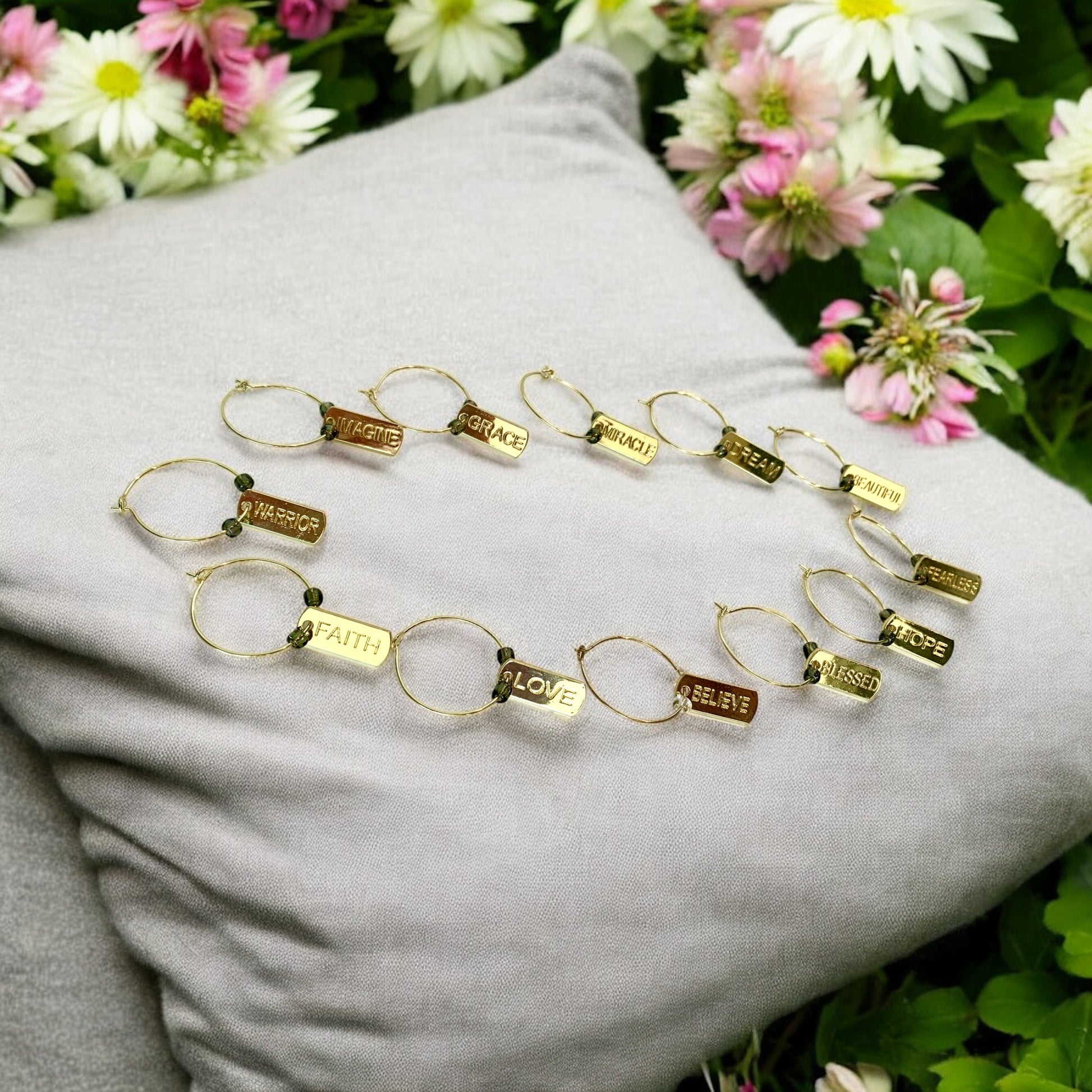 Gold wine glass charms with engraved words on a gray surface with flowers in the background