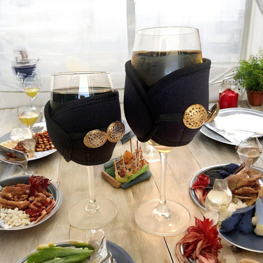 Two wine glasses with decorative black holders on a table with food and drinks.